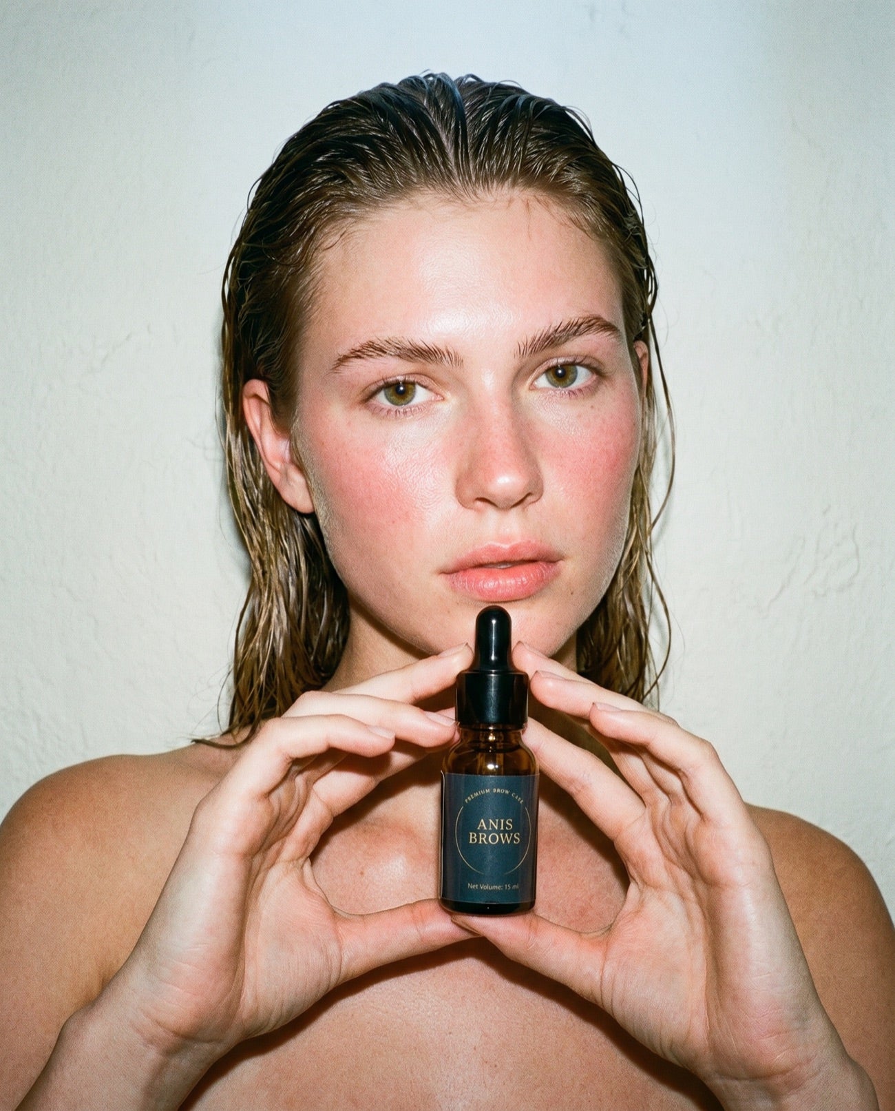 Model with dewy skin holding the Anis Brows serum